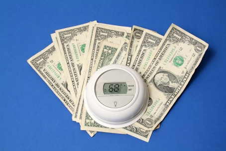 A thermostat sits on a pile of one-dollar bills, set to 68 degrees