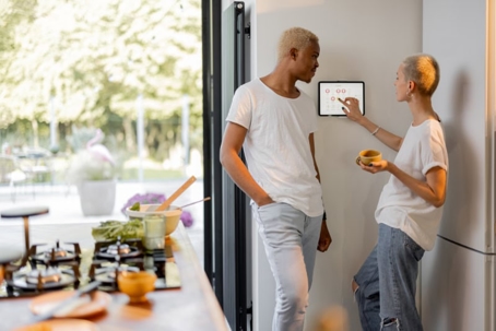 In a bright kitchen, a young couple is setting their smart thermostat.