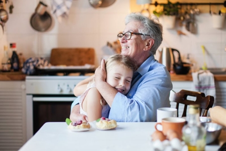 A grandmother hugs her granddaughter at a kitchen table with pastries.