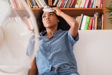 A woman holds a cool cloth to her forehead, seeking relief from the heat with the help of a fan.