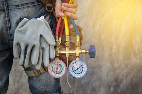 HVAC technician with a gauge manifold set and gloves, ready for AC repair.