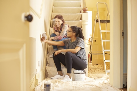 Two people sit on stairs covered in drop cloths, picking a paint color for their home's interior.