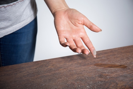 A hand shows collected dust from a dark wood surface.