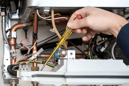 A technician services a tankless water heater, using a yellow-handled screwdriver to inspect the inner-workings of the unit.